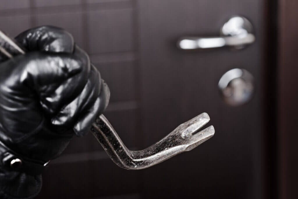 A hand holding crowbar about to tamper with a door lock.