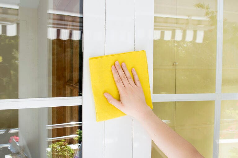 A person cleaning an aluminum window frame with a yellow rag