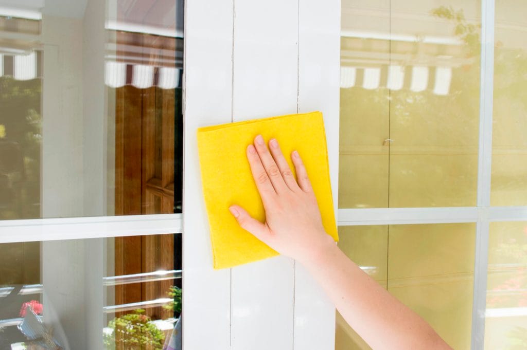 A person cleaning an aluminum window frame with a yellow rag