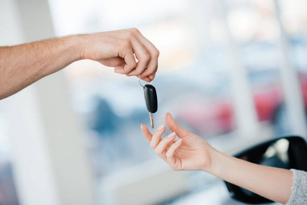 A Person Handing A Car Key To Another Person