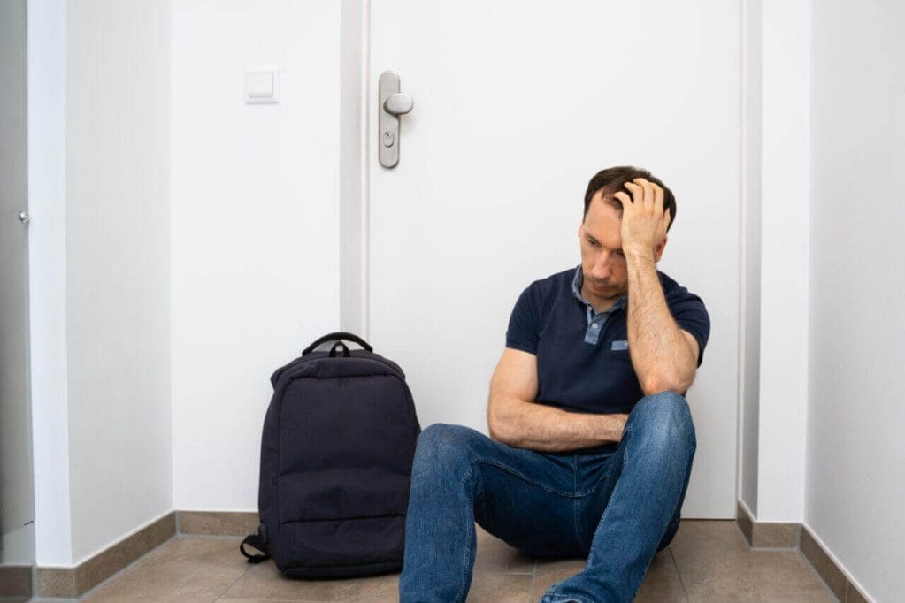 A Stressed Person Sitting Next To A Locked House Door