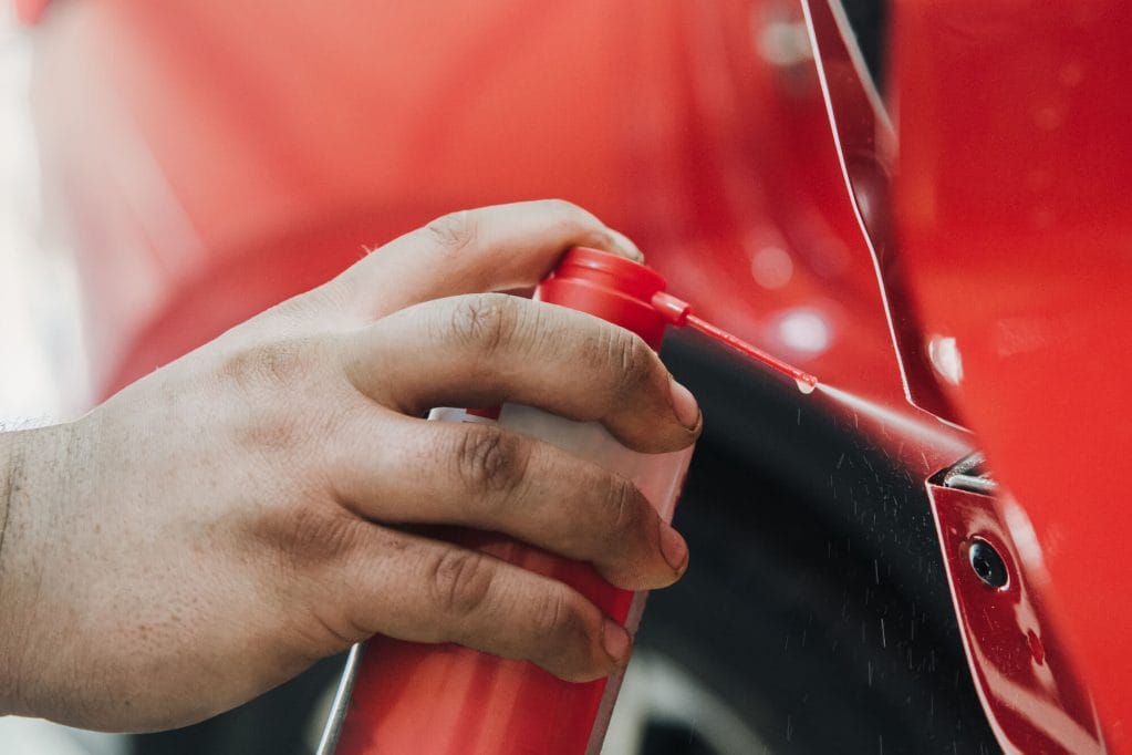 Close up of a person spraying lubricant into car door mechanisms